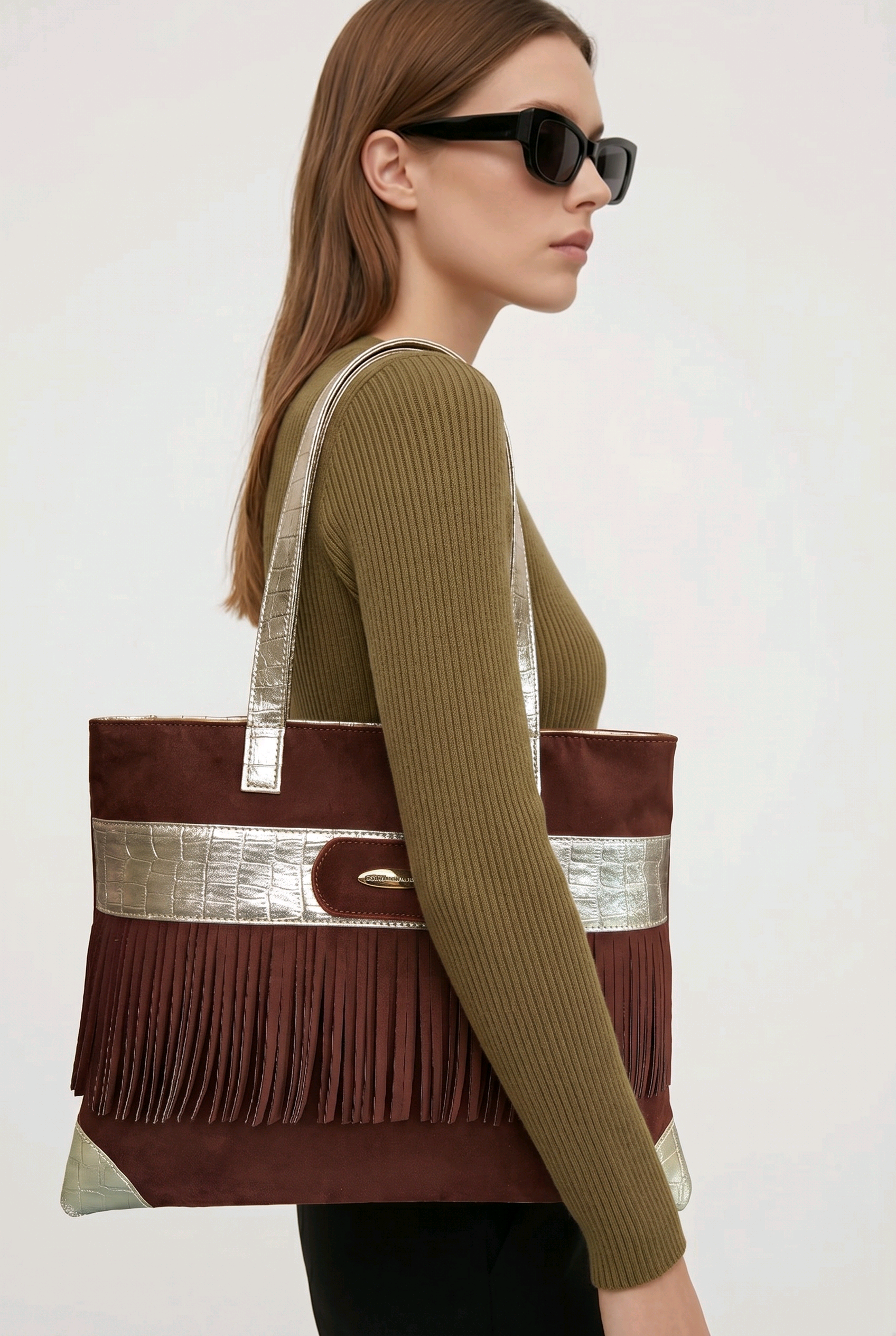 Model wearing a brown suede shoulder bag featuring metallic crocodile embossed trim and long fringes, designed by Ilaria Ricci for Rita Cordini.