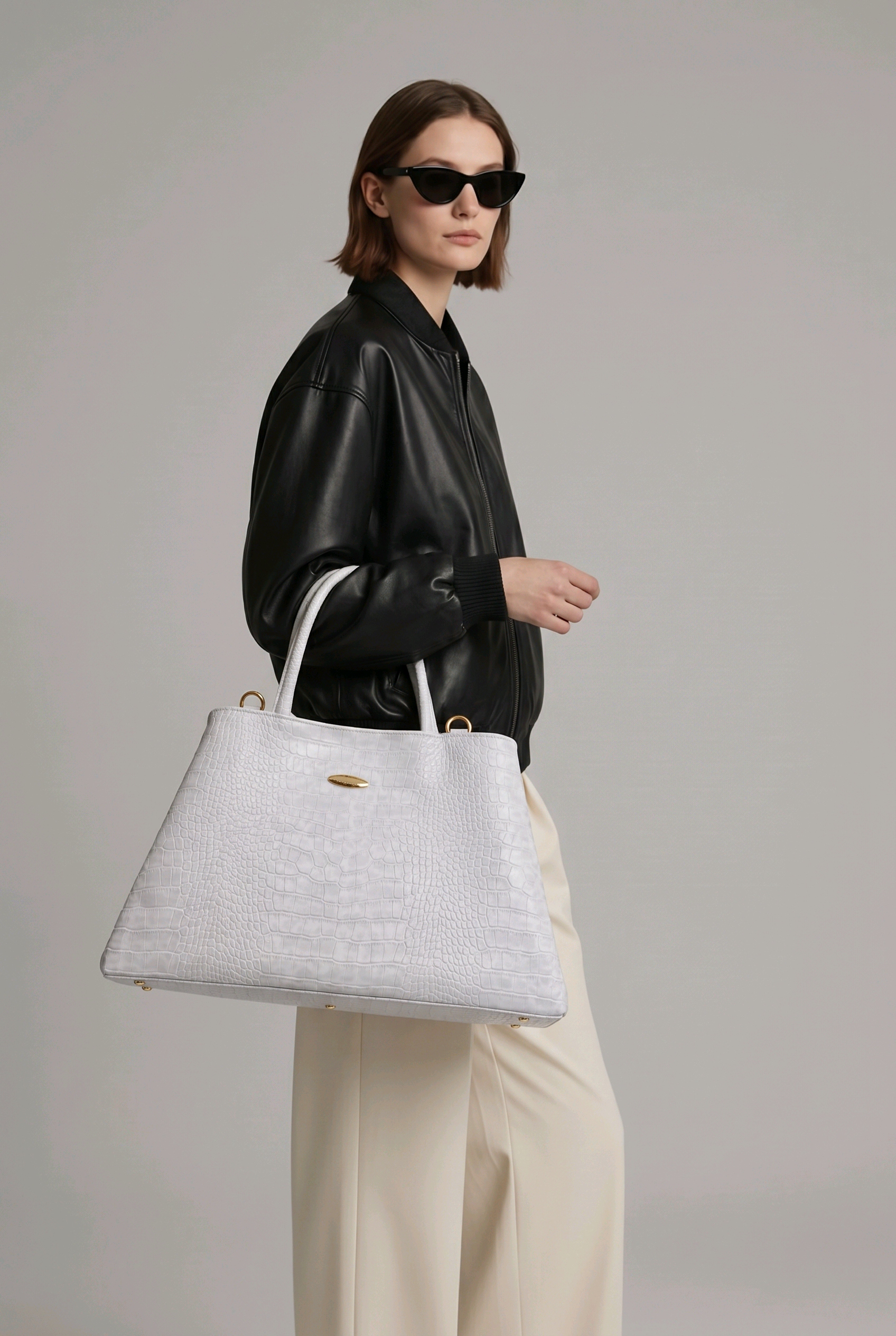 Model in a black leather bomber jacket carrying a large white crocodile embossed tote bag from the Rita Cordini Jungle Rock collection.